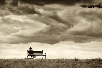 One woman sits on a bench and looks at the sea. Line horizon and earth on the background of beautiful clouds. Horizontal frame. Sepia.
