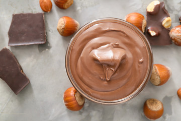 Bowl with tasty chocolate paste and hazelnuts on grey background