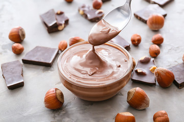 Bowl and spoon with tasty chocolate paste and hazelnuts on grunge background