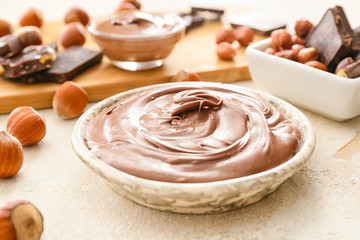 Plate with tasty chocolate paste and hazelnuts on light background