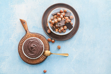Fototapeta premium Plates with tasty chocolate paste and hazelnuts on color background