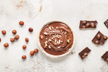 Bowl with tasty chocolate paste and hazelnuts on light background