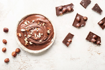 Bowl with tasty chocolate paste and hazelnuts on light background