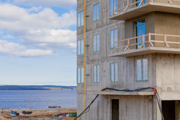 A construction site by the lake and a new house made of concrete and metal. The construction of a skyscraper.