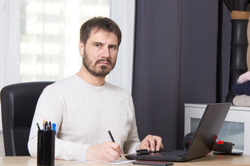 a bearded man is sitting at a Desk looking for work calling on his mobile