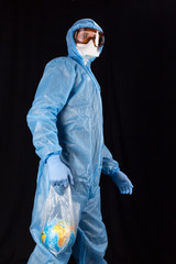 portrait of a man in a chemical protection suit, medical gloves, a mask and glasses holds a package with the planet Earth inside on a dark background