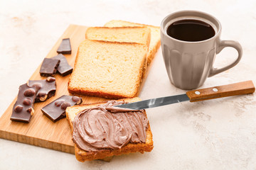 Fresh bread with chocolate paste and cup of coffee on light background