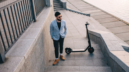 Young hipster man in a suit riding an electric scooter in bright sunny day. Ecological transportation concept.