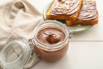 Jar with chocolate paste and bread on table
