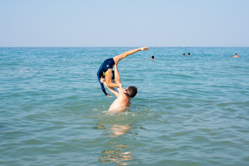 Father, playing with child at the seaside. Executing water jumps.