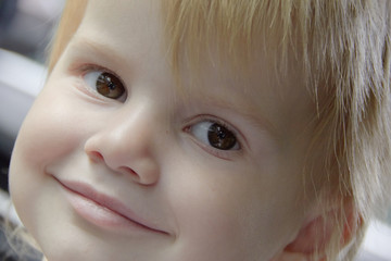 Close up of the face of a smiling little girl with blond hair in a car