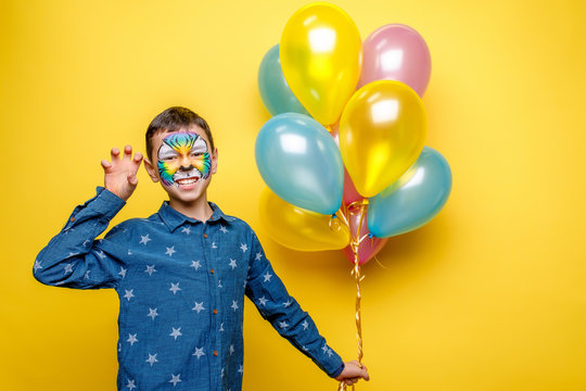Happy boy with aquagrim on birthday party, colorful tiger holding colorful balloons isolated on yellow background - Powered by Adobe