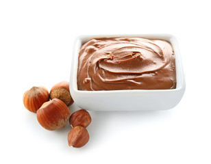 Bowl with tasty chocolate paste and hazelnuts on white background