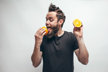 Young bearded hipster man holding slices of orange in front of his eyes. Crazy emotions
