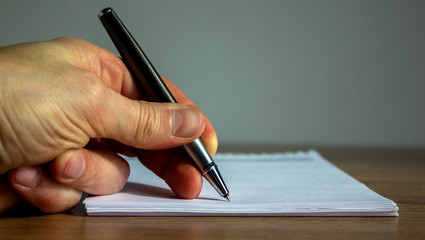 Notebook and fingers of a working man with a pen on wood table.