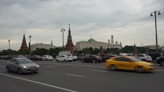 
View of passing vehicles from the Bolshoy Kamenny Bridge on a cloudy day. The Grand Kremlin Palace and The Ensemble of a Belltower of Ivan in the background.