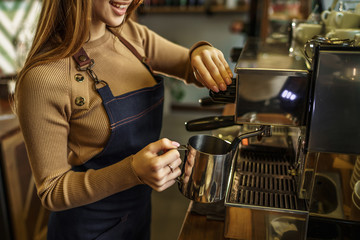 Cropped photo, young girl, barista steaming milk at the modern coffee shop