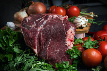 A piece of raw meat on a wooden cutting Board and various vegetables. Cooking meat. Fresh beef and ripe vegetables. Balanced diet. Natural protein.
