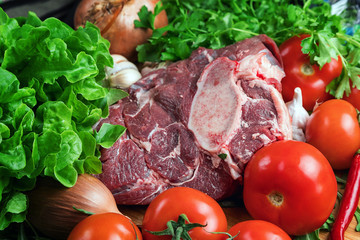 The preparation of fresh meat. Fresh beef steak on a wooden table. Meat surrounded by spices and vegetables. Fresh fruit. Red ripe tomatoes. Dietary food.