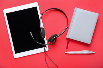 Tablet computer with headset and notebook on color background