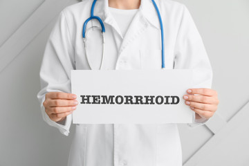 Doctor holding paper with word HEMORRHOID on light background