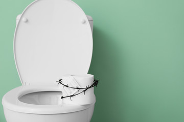 Toilet bowl with roll of paper and barbed wire on color background. Hemorrhoids concept