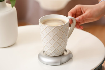 Woman taking cup of coffee from heater on table
