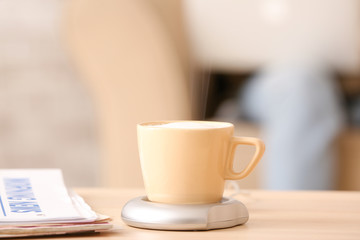 Cup of coffee with heater and newspaper on table