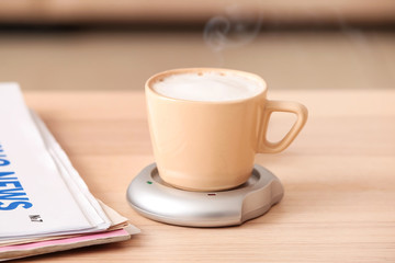 Cup of coffee with heater and newspaper on table