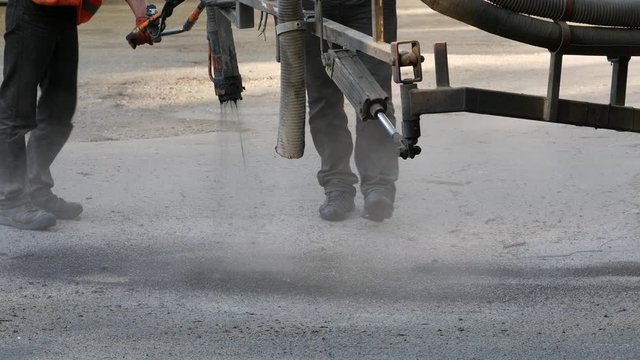 Workers perform minor repairs to pavement by spraying asphalt chips into pits on roadway. Machine blows hot bitumen mixture as road patches. Sealing cracks by blowing crushed granite stone with tar 