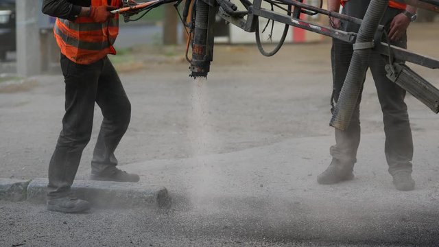 Workers perform minor repairs to pavement by spraying asphalt chips into pits on roadway. Machine blows hot bitumen mixture as road patches. Sealing cracks by blowing crushed granite stone with tar 