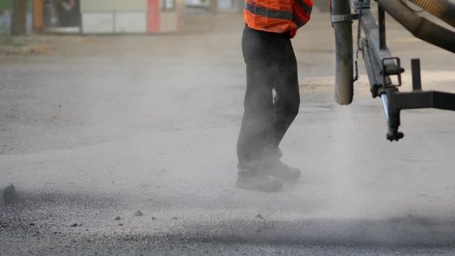 Workers perform minor repairs to pavement by spraying asphalt chips into pits on roadway. Machine blows hot bitumen mixture as road patches. Sealing cracks by blowing crushed granite stone with tar 