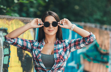 Beautiful fashion young woman in retro sunglasses posing near graffiti wall