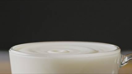 Milk drops drip into a cup with organic milk making splash around a dark background. Slow motion, Full HD video, 240fps, 1080p.