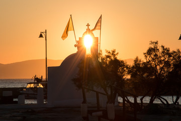 Sonnenuntergang am Hafen von Naxos, die Sonne scheint durch eine Öffnung im Turm eines Monoments