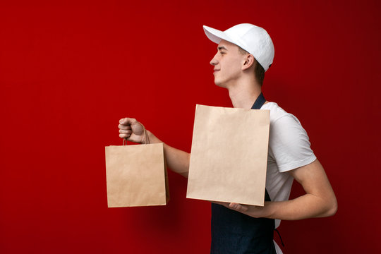 cheerful courier gives packages with an order and smiles, delivery man holds parcels on a red background