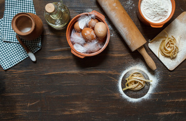 Freshly prepared dry tagliatelle on a Board with flour, and ingredients for cooking pasta, dark background, top