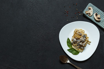 Homemade pasta with mushrooms and sauce on a white plate, black background , top view