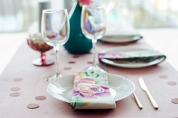 Guest place, table setting in dusty pink colors with beautiful white dishes, golden cutlery, confetti, glasses of wine. Close up. elective focus.