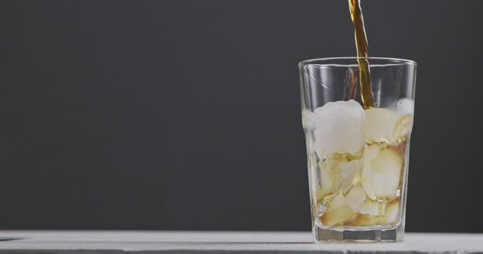 In a glass with ice pour coffee with splashes and bulbaki around a dark background. Slow motion, 2K UHD video, 1080p.