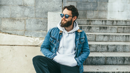 Obraz premium City portrait of handsome hipster guy with beard wearing gray blank hoodie or hoody with space for your logo or design. Mockup for print