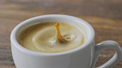 Close-up in a cup of fragrant espresso with foam fall coffee splash on a brown wooden table. Slow motion, Full HD video, 240fps, 1080p.