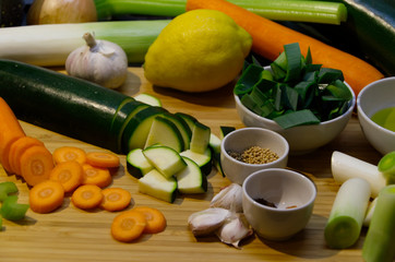 Chopping board with leek, zucchini, carrots, celery sticks, onion, garlic, lemon, olive oil & spices