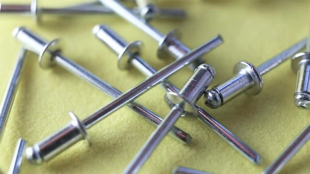 Aluminum rivets fall down. Extreme close-up, real time, on a yellow background