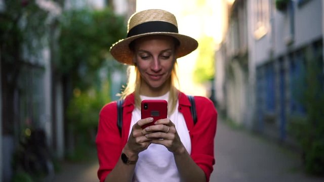 Slow motion with soft focus of cheerful female walking on city street with smartphone gadget in hands enjoying sunny day, happy hipster girl texting message in mobile phone. Cellphone application 

