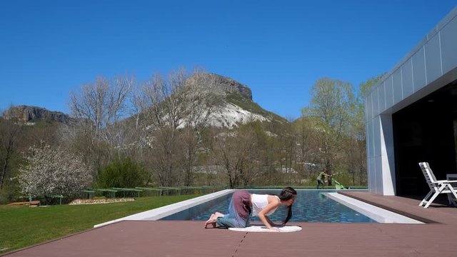 Yoga. By the pool. The girl with long dark hair doing yoga. Open air stretch