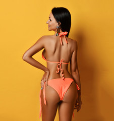 Young beautiful smiling tanned slim brunette woman in sexy orange bikini standing backwards