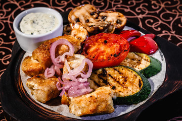 Wooden plate with meat, roasted vegetables and sauce.