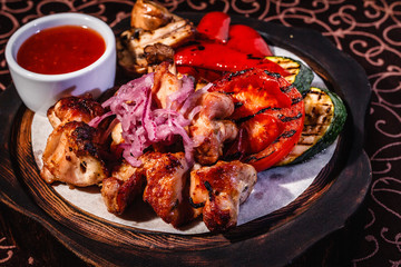 Wooden plate with meat, roasted vegetables and sauce.