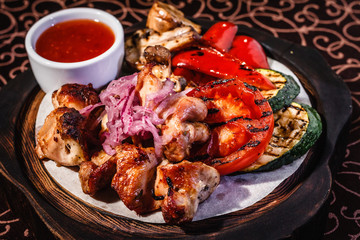 Wooden plate with meat, roasted vegetables and sauce.